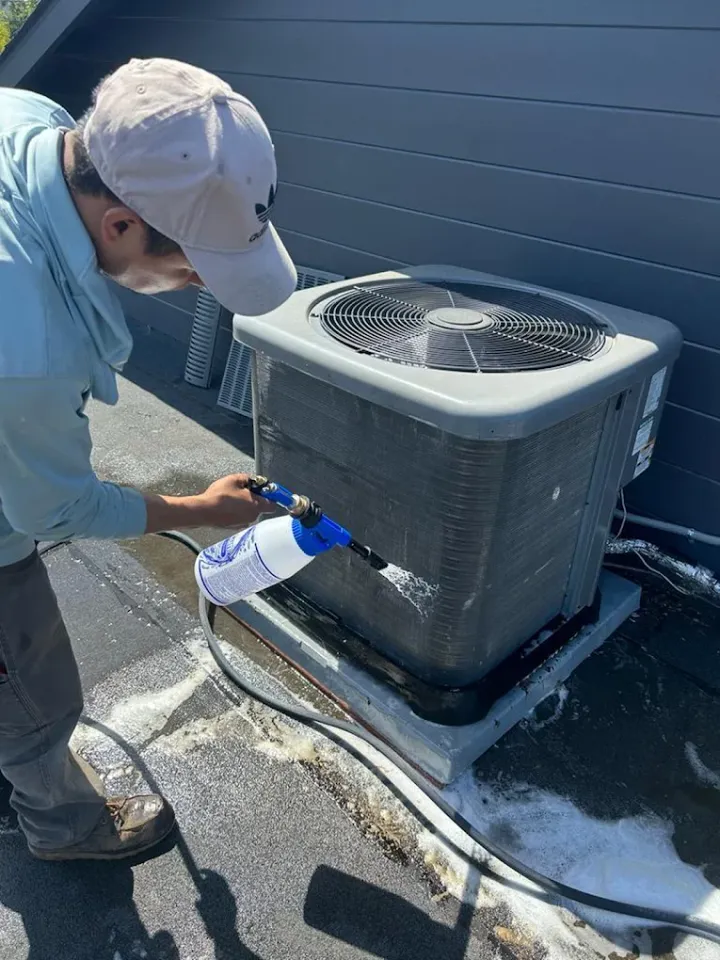 Technician cleaning an outdoor air conditioning unit