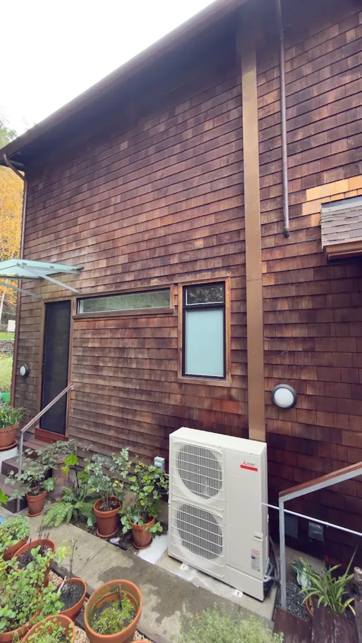 Outdoor mini-split unit beside a wood-sided home